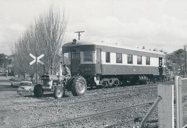 A man is driving a tractor in a rail yard, pulling a railway carriage along a track over a crossing.