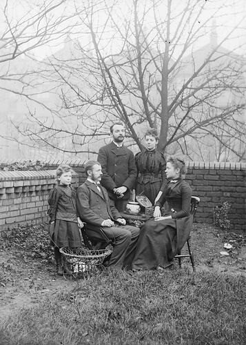 Two men, two women and a young boy pose around a table in a walled garden.