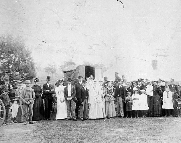 Group of people in formal clothes in front of buggies and house.