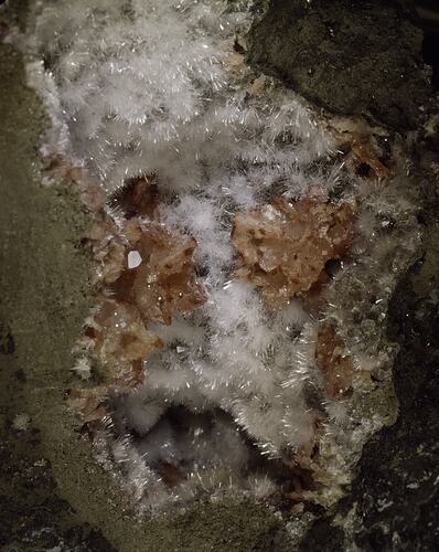 Blocky orange and needle-like white crystals on a grey rock.