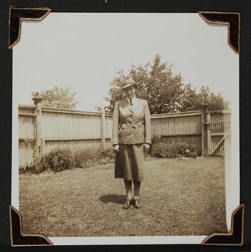 Woman in uniform standing in a yard with fence behind.