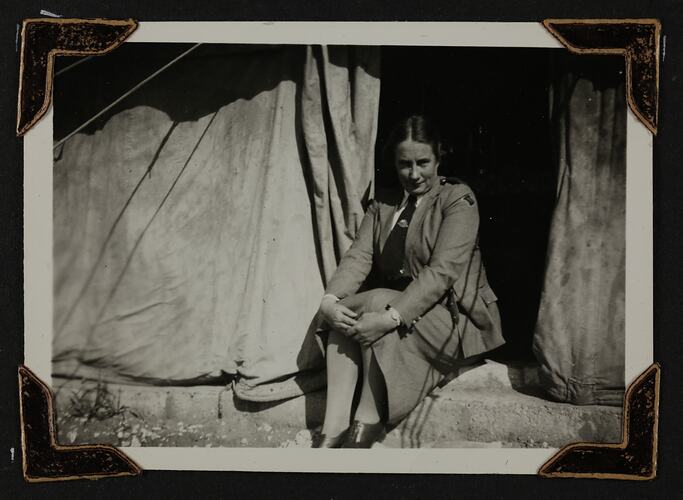 Women in uniform sitting outside tent.