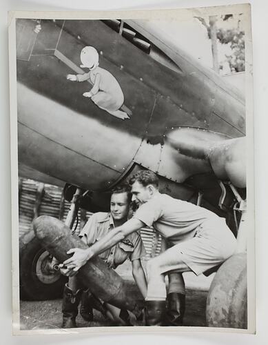 Two men holding a bomb next to a plane with baby painted on side.