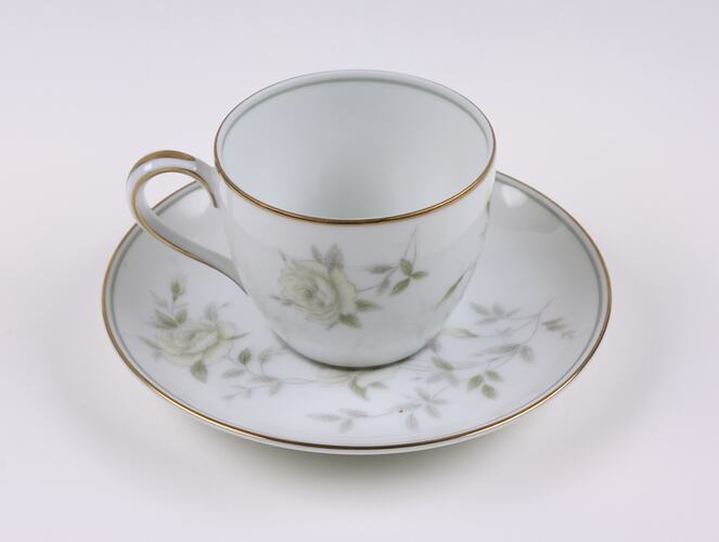 White china cup and saucer with flower pattern and gold rim.