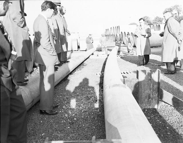 Monochrome photograph of men testing cement pipes.