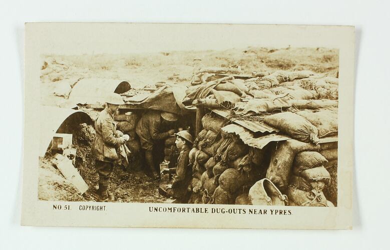 Three servicemen in trench with sandbag walls.