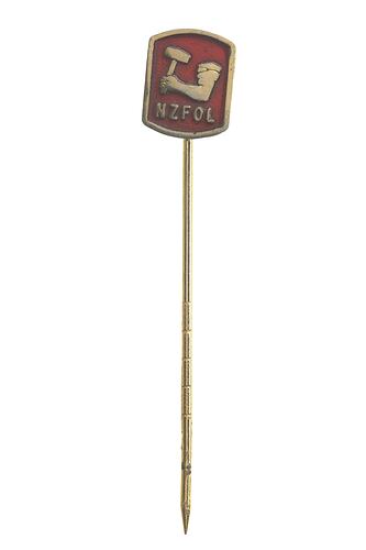 Red square stick pin with raised letters NZFOL beneath an arm, in a rolled up shirt sleeve, holding a mallet.