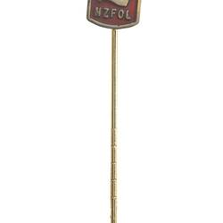 Red square stick pin with raised letters NZFOL beneath an arm, in a rolled up shirt sleeve, holding a mallet.