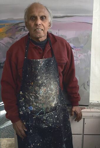 Man wearing painted splattered apron stands in front of artwork.