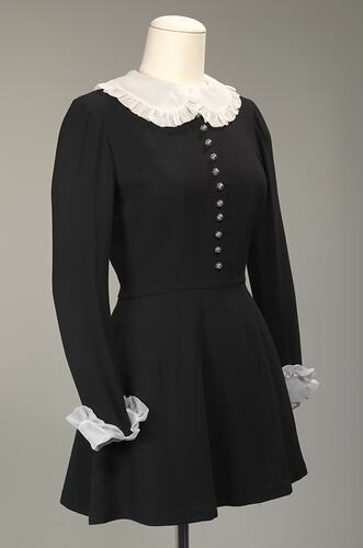 Angle view of long sleeved black wool mini dress. White collar and cuffs.