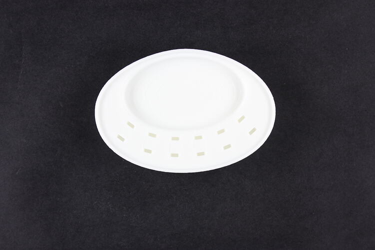 Bottom view of white plastic, oval, rounded device with twelve holes.