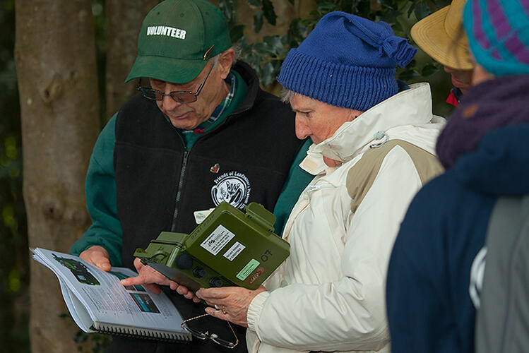 Three people in coats and hats looking at equipment and manual outside.