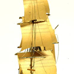 Front view of three masted ship with wooden hull.