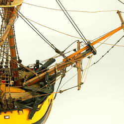 Detail of bowspirit on model ship with wooden hull painted yellow.