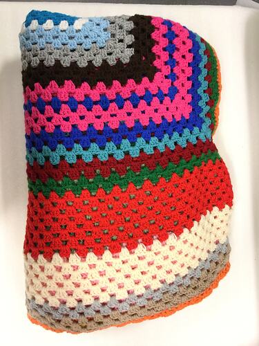 Folded, multicoloured, woolen crocheted blanket.