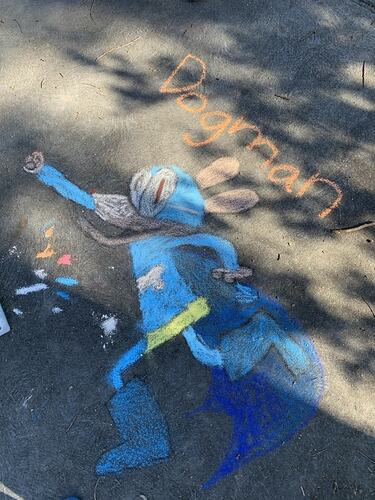 Blue chalk drawing of the 'Dogman' superhero character on a driveway.