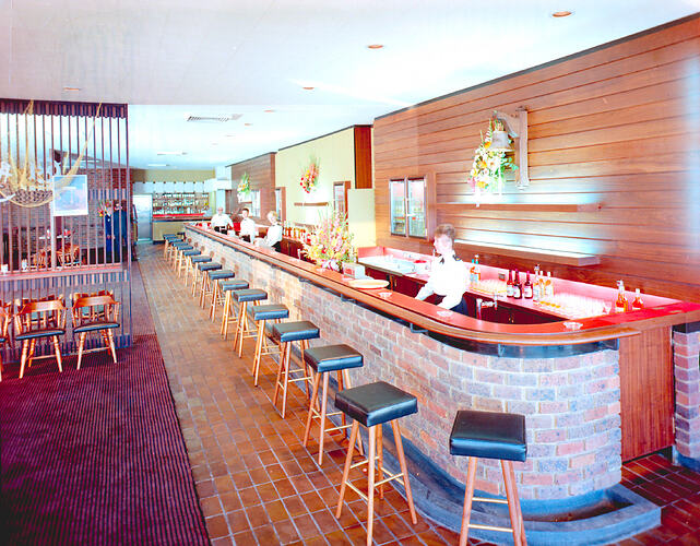 Male and female bartenders stand behind a hotel bar  which is decorated in a nautical theme. They wear nautical-style uniforms.