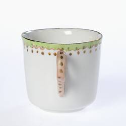 White tea cup with green, pink and gold decorated rim. Gold painted handle. Handle view.