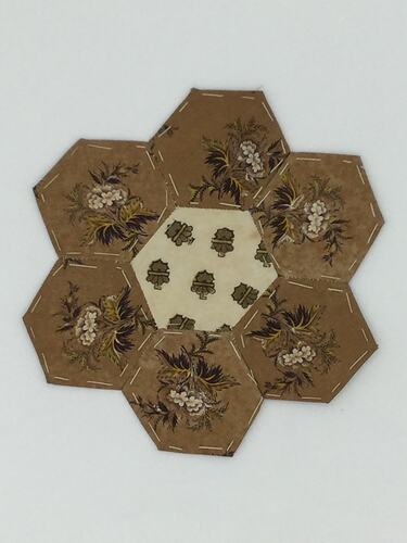 Brown hexagonal coloured fabric patches that are stitched together. Cream centre.