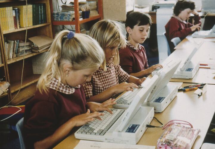 Primary school students in school uniform, working on laptops.