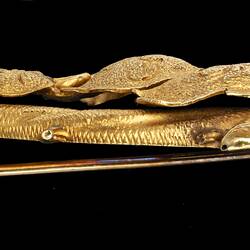 Profile of ornate gold brooch with vine leaves on a branch.