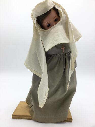 A doll dressed as a nun in a grey dress and white veil