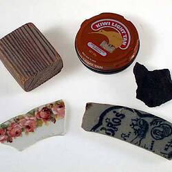 Five hopscotch taws; wood block, shoe polish tin, rock, 2 pottery shards.