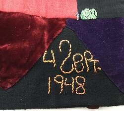 Detail of embroidered yellow lettering on dark section of multicoloured patchwork skirt.