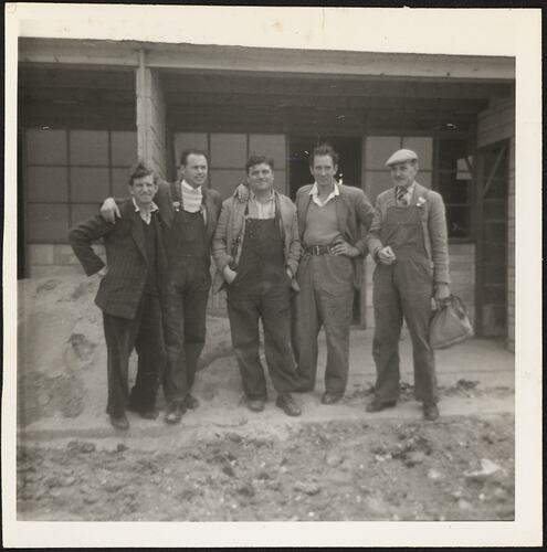 Man standing with four workmates on a buidling site. Building behind them.