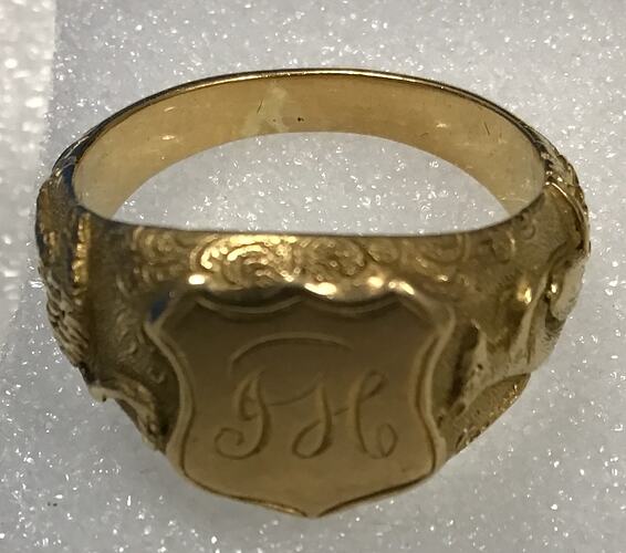 Gold ring with a shield featuring engraved initials.