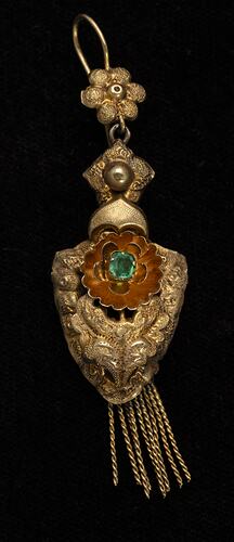 Gold and green paste pendant earring. Comprised of four connected sections with floral and leaf motifs. Gold fringe hangs from the bottom.