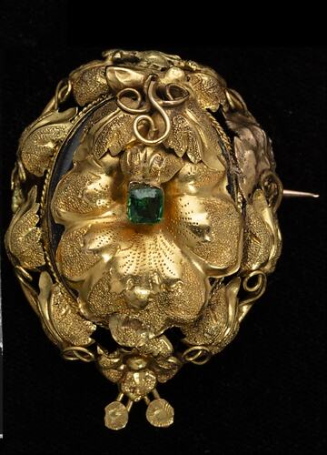 Round gold brooch with leaves and tendrils. Green paste stone in centre.