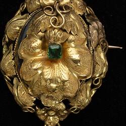 Round gold brooch with leaves and tendrils. Green paste stone in centre.