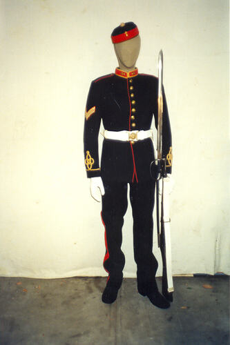 Mannequin holding rifle in dark blue military uniform with red and yellow trim.