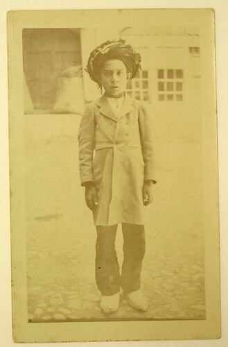 Boy with headdress standing in front of building.
