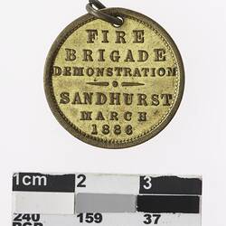 Round gold coloured medal with text.