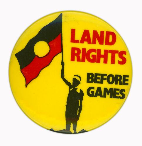 Round badge, yellow with red and black text. Figure holds Aboriginal flag.