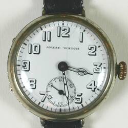 Watch, detail. Circular white dial, skeleton Arabic numerals, brown leather bands.