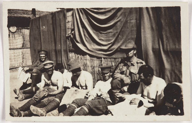 Group of servicemen sitting in front of a structure made of reeds with fabric draped over it.