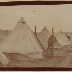 Two servicemen at a campsite with conical tents.