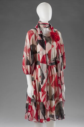 White, red, and black pattered dress with neck-scarf.