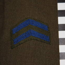 Patch with two blue chevrons stitched onto green felt on Khaki wool fabric.