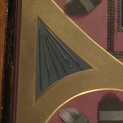 Detail of panel made of needles, crochet hooks, surgical needles, and other needles and needle cases. In red, black and yellow.