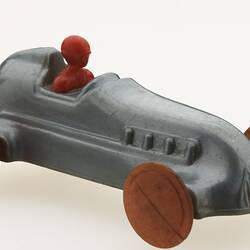 Silver racing car with red driver, front view.