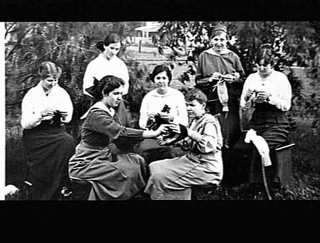 Group of women sitting outside knitting.