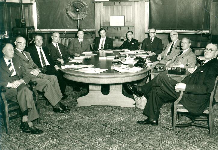 Group of men sitting around board room table.