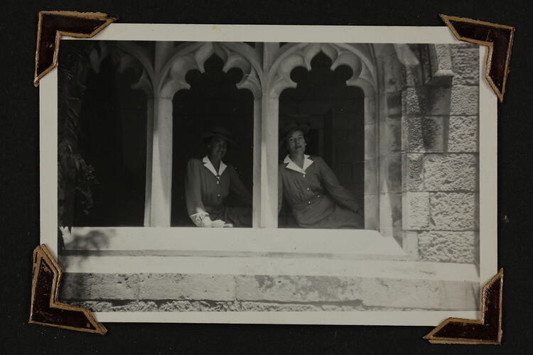 Two woman sitting in window arch of stone building.