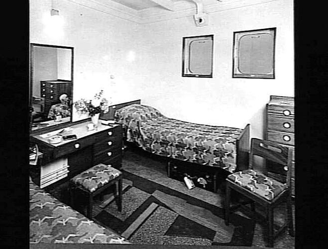 Ship interior. Two single beds against each wall. Dressing table and chairs in between.