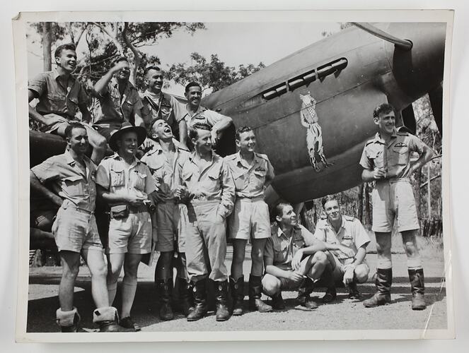 Group of airmen posed by an aircraft with artwork painted on side.