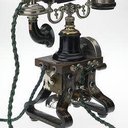 Iron telephone painted black with gold details. Two fork support on top for receiver. Green plaited cords.